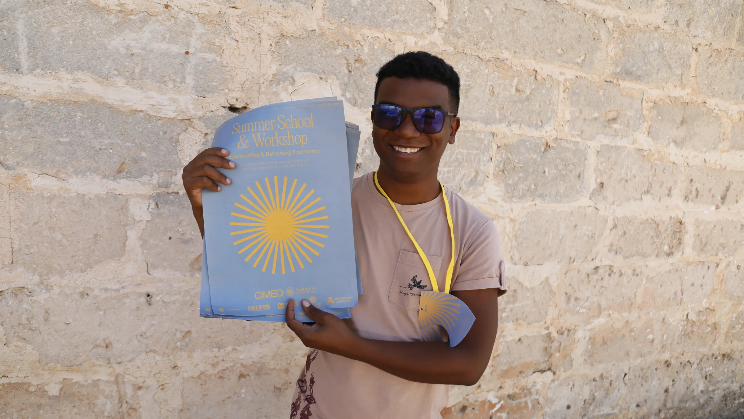 Participant holding a stack of summer school posters with the yellow sun